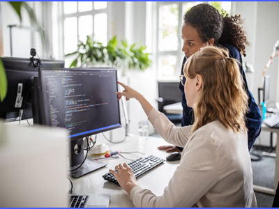 two people in front of a computer monitor with one person pointing to the monitor