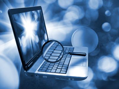 laptop with a magnifying glass suspended over the keys with blurred circles in various hues of blue and white in the background